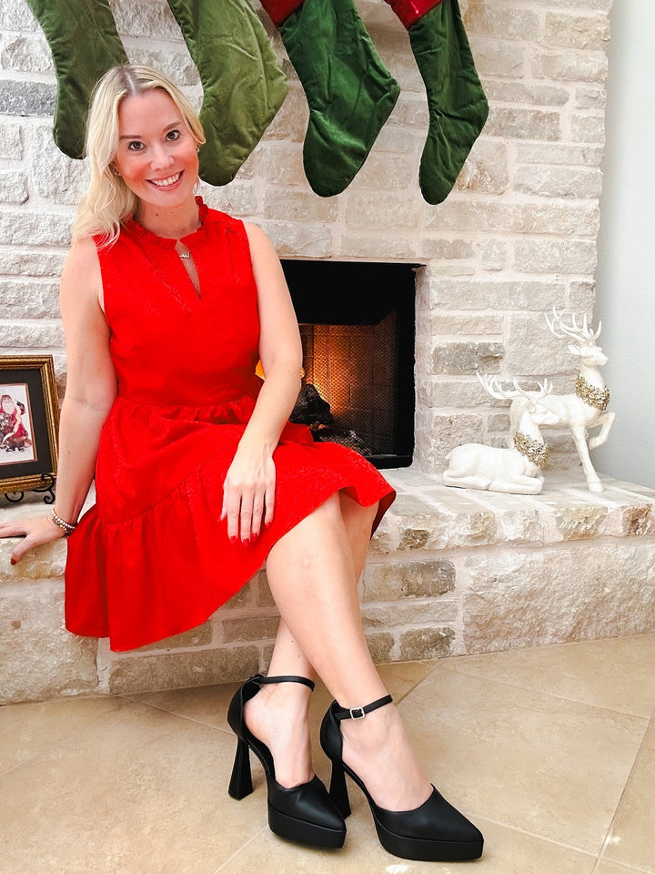 Woman in a red dress sitting in front of a fireplace with stockings hanging above.#color_black-pu