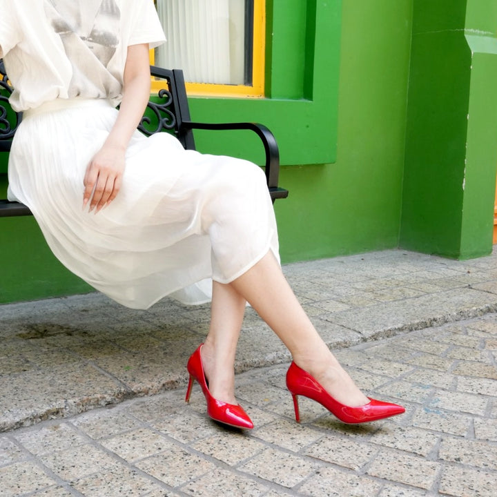 Person wearing a white dress and red high heels sitting on a bench with a green wall in the background.#color_red