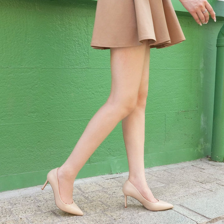 Person wearing beige high heels and a skirt against a green wall.#color_natural