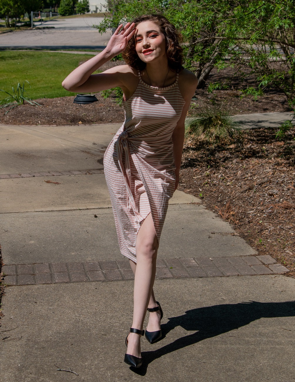 Woman in a patterned dress standing on a sidewalk with trees and grass in the background#color_black