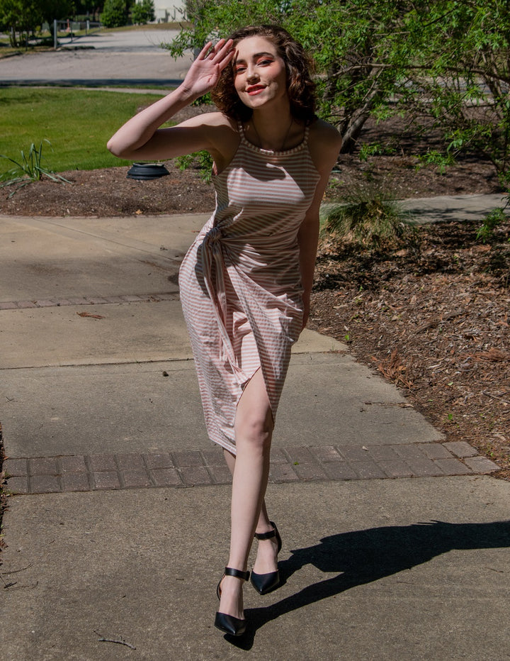 Woman in a patterned dress standing on a sidewalk with trees and grass in the background#color_black