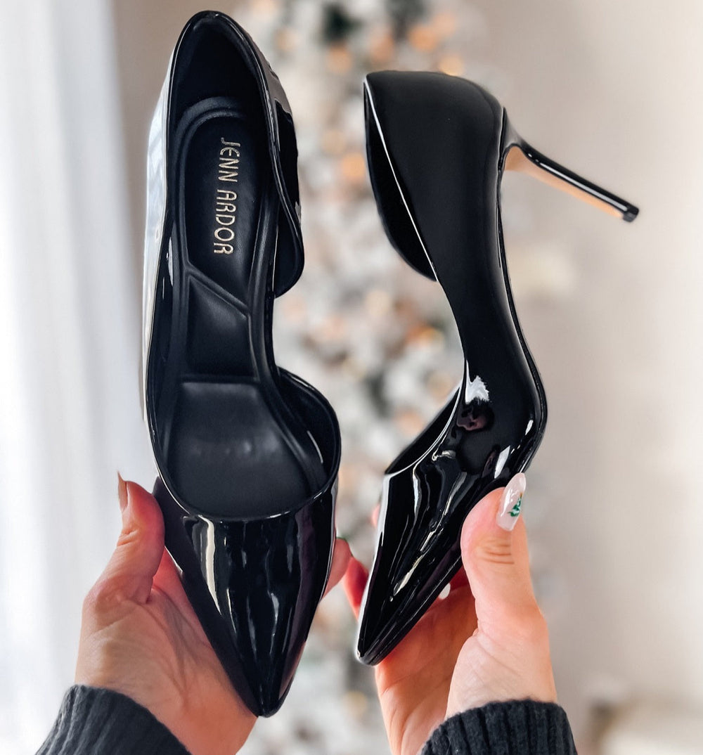 Black high-heeled shoes held by a person with a blurred background.#color_black