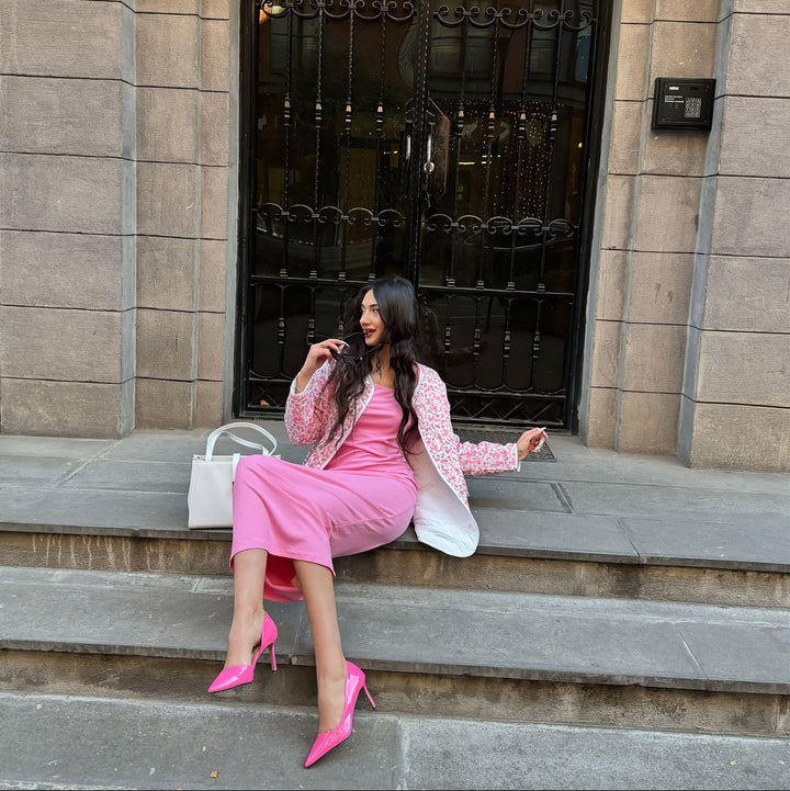 Woman in a pink dress and heels sitting on steps in front of a building entrance.#color_pink