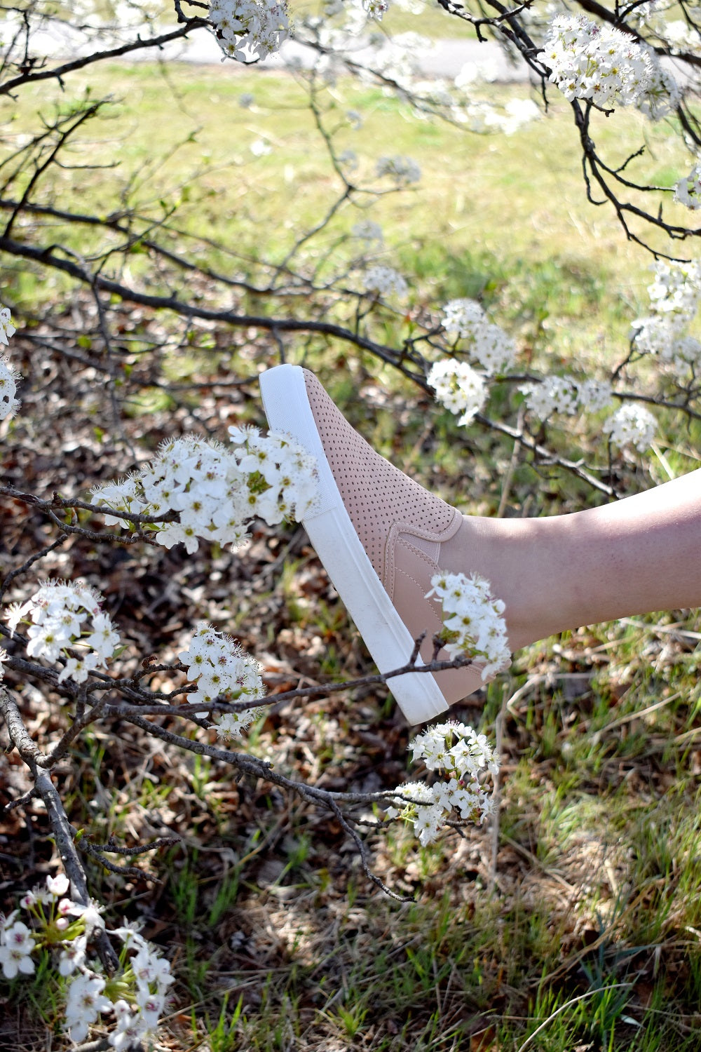 Person wearing a light pink sneaker stepping over white flowers with a natural background#color_pink
