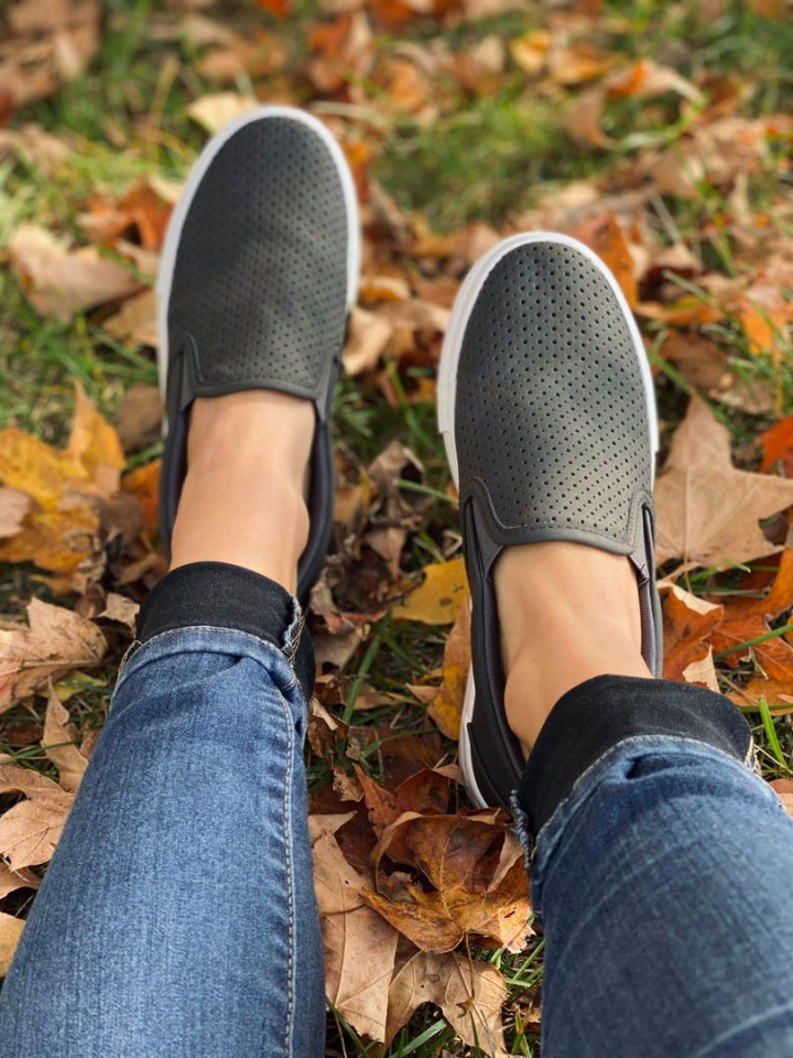 Gray slip-on shoes worn with blue jeans on a grassy ground with fallen leaves.#color_black