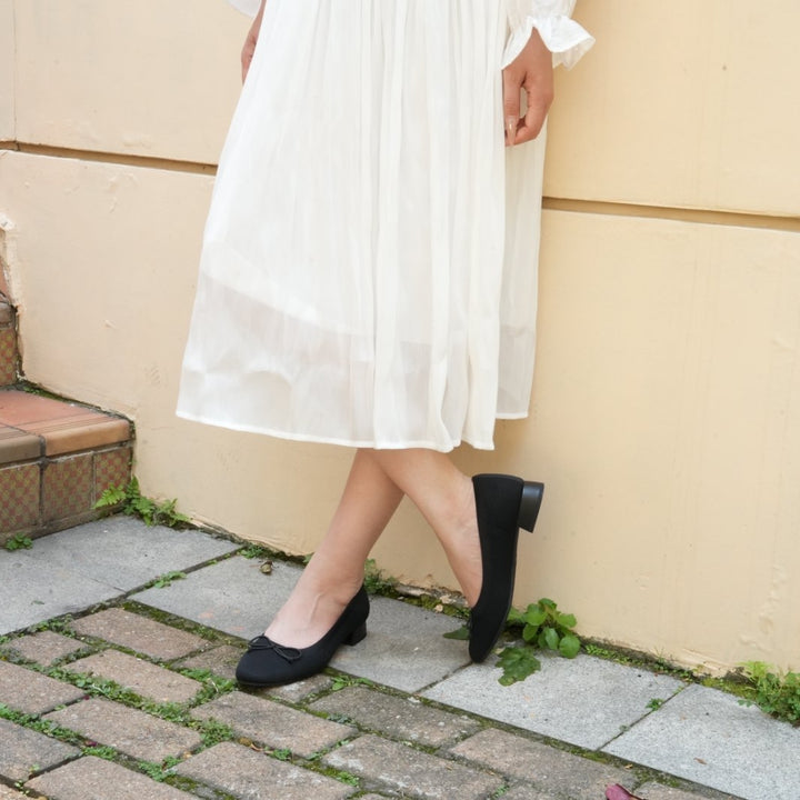 Person wearing a white dress and black shoes standing on a stone path.#color_black