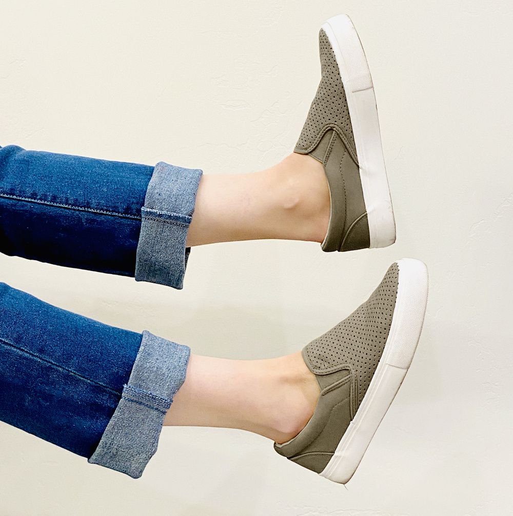 Beige slip-on shoes worn with rolled-up blue jeans on a light background#color_grey