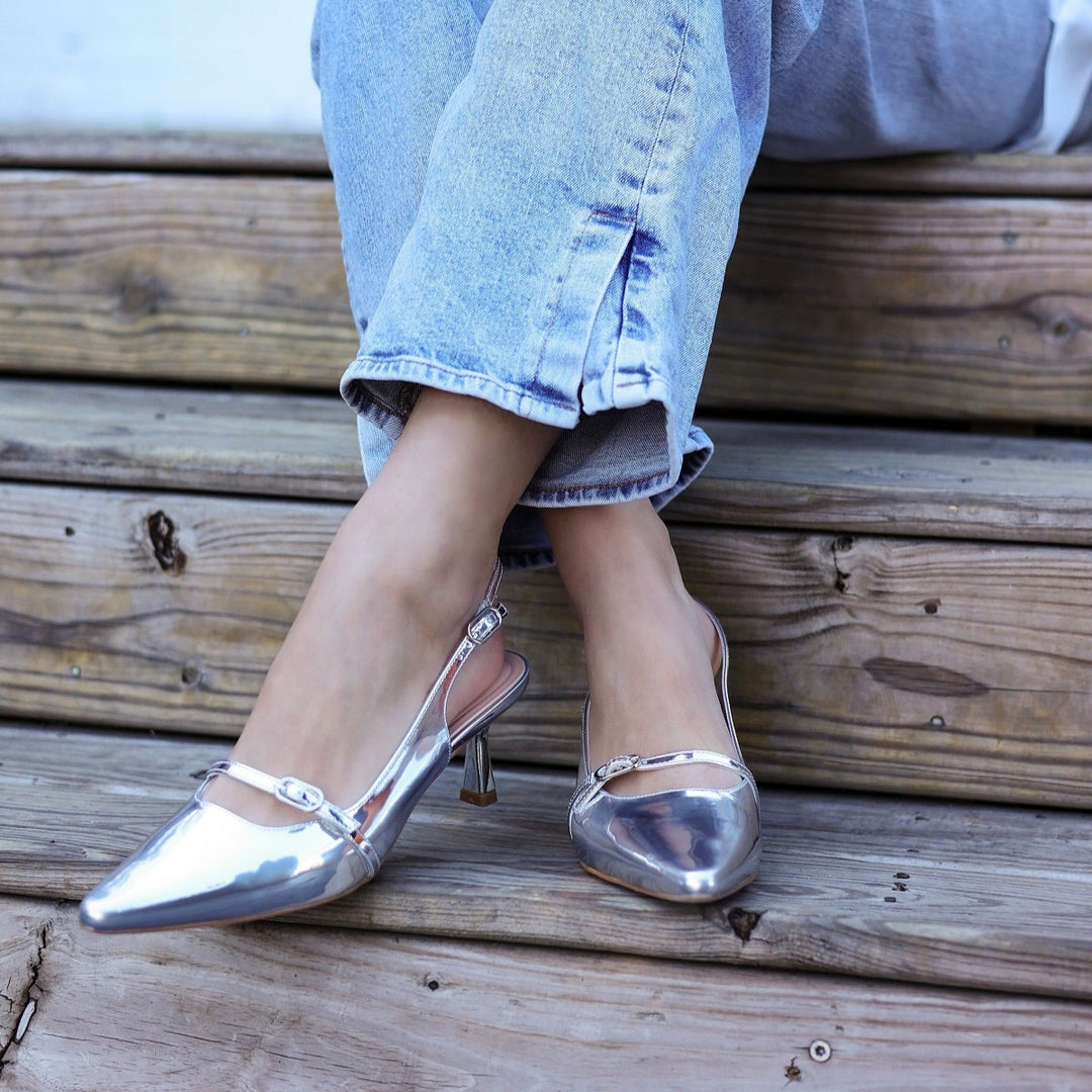 Person wearing silver metallic shoes and light blue jeans sitting on wooden steps.#color_silver