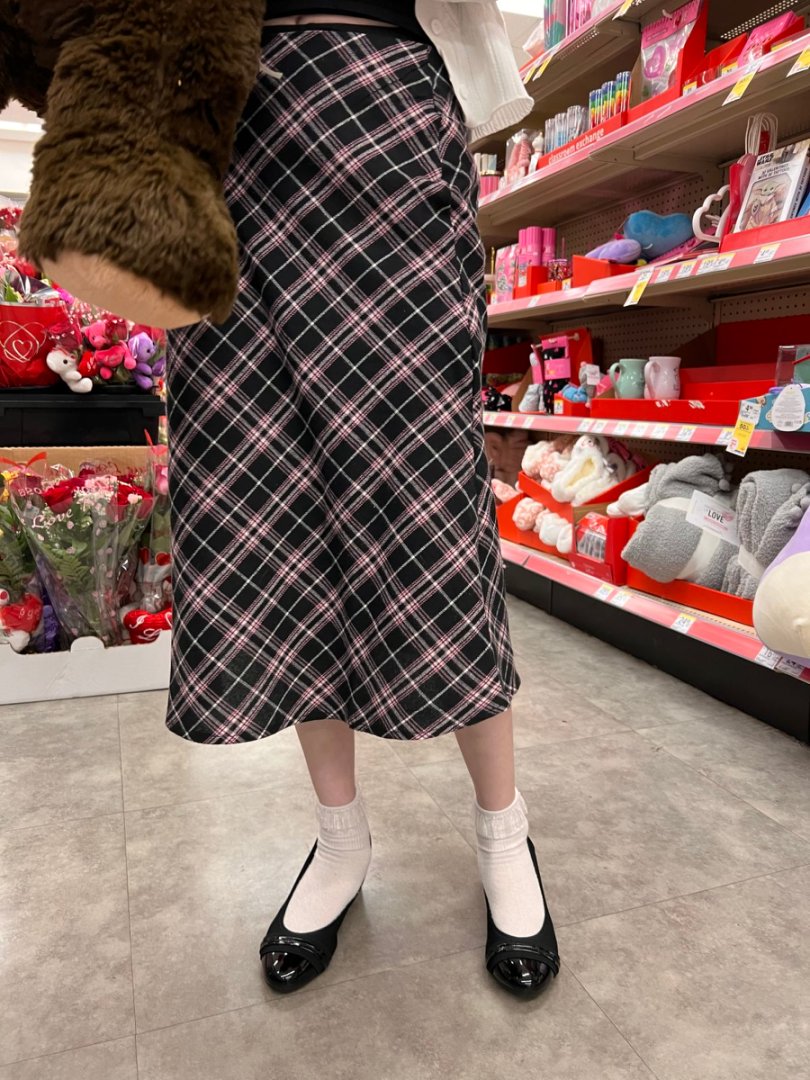 Person wearing a plaid skirt in a store aisle with toys and products on shelves.#color_black1