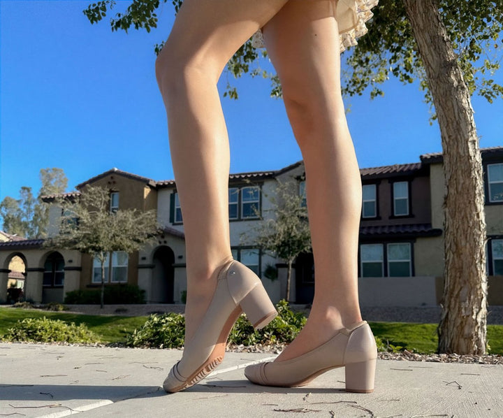 Person wearing beige high-heeled shoes standing on a sidewalk with a residential background#color_natural