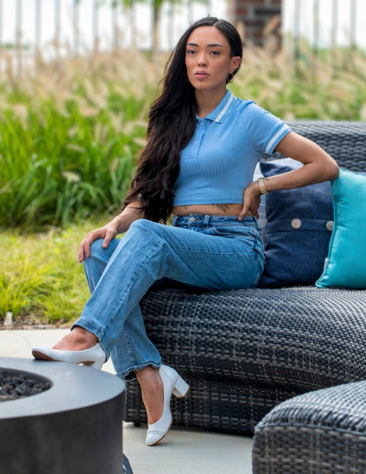 Woman sitting on a outdoor sofa wearing a blue top and jeans, with a garden background.#color_white