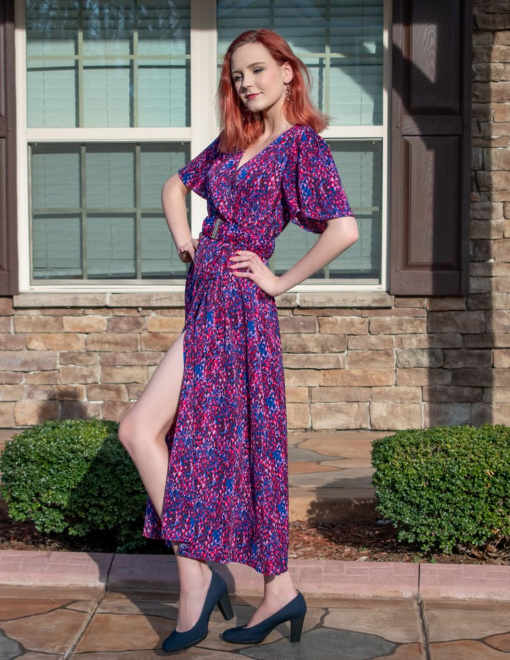 Woman in a purple floral dress standing outside a house.#color_navy