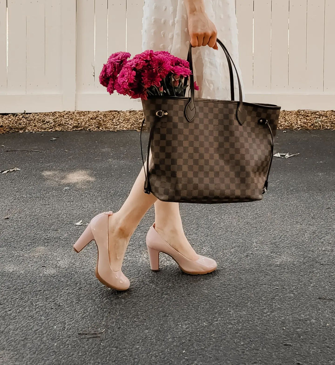Person walking on a pavement holding a patterned handbag with pink flowers.#color_natural