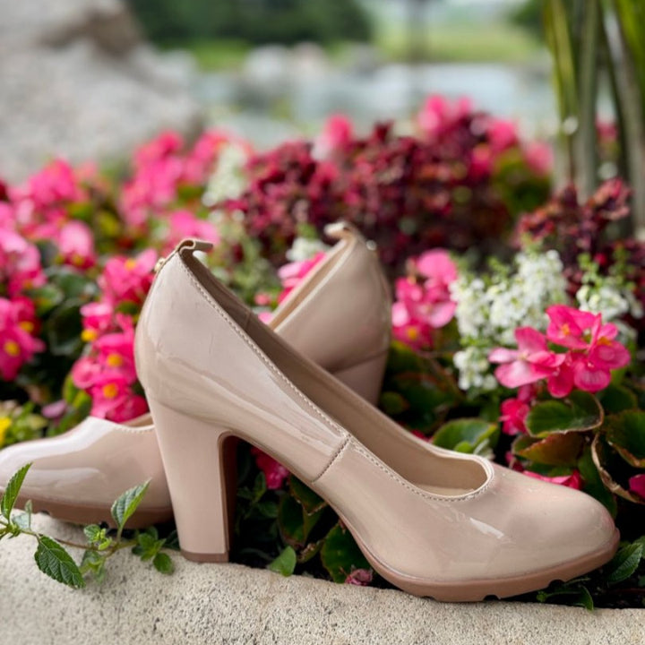 Beige high-heeled shoes on a stone surface with flowers and blurred nature in the background.#color_natural