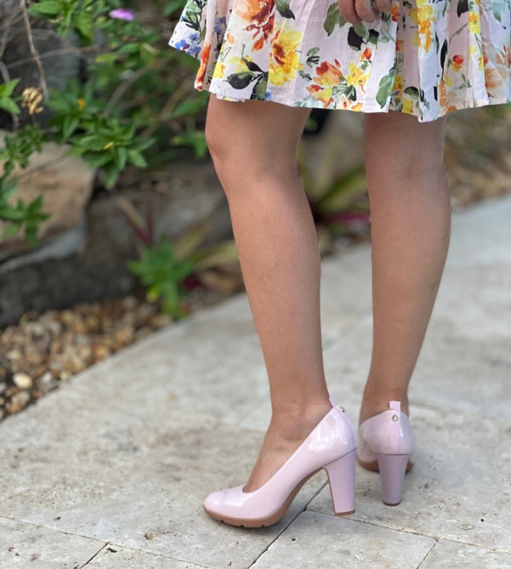 Person wearing pink high-heeled shoes and a floral dress on a stone path.#color_pink