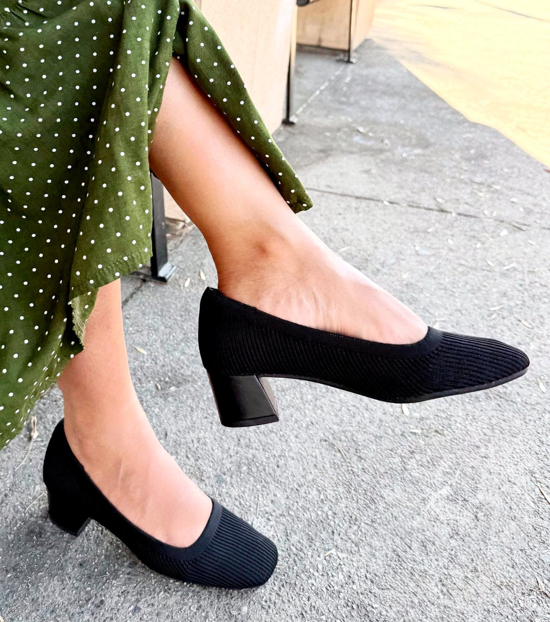 Person wearing black shoes and a green polka dot skirt on a sidewalk.#color_black