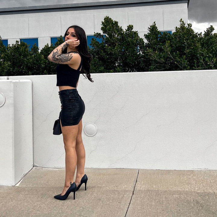 Woman in a black outfit standing against a white wall with a cloudy sky.#color_navy