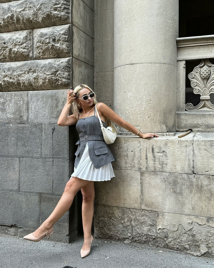 Woman in a gray dress and sunglasses styling slingback kitten heels leaning against a stone wall.#color_nude