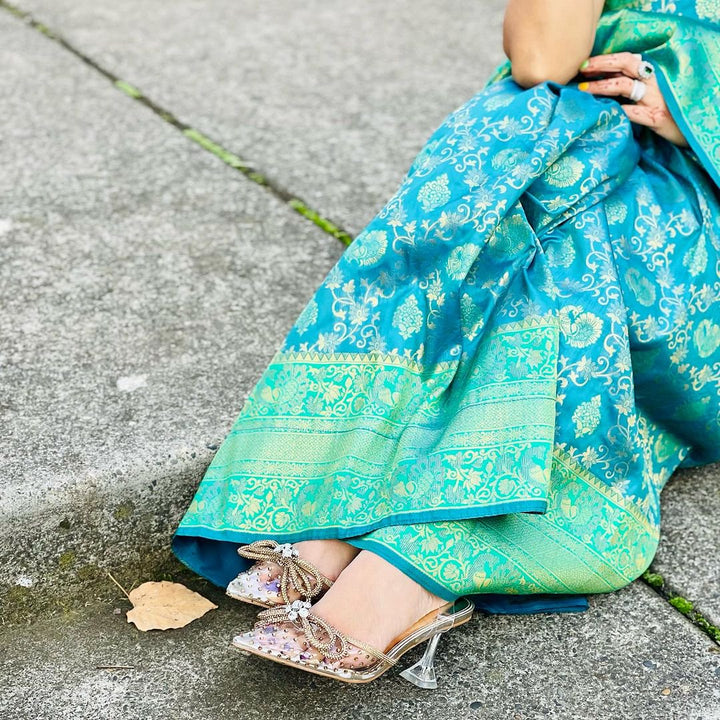 Person wearing a blue and green patterned saree sitting on a concrete surface.#color_gold-rhinestone