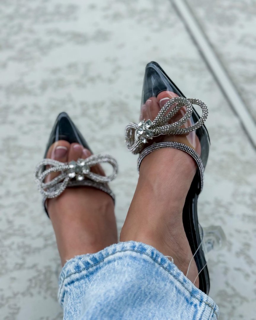 Black high-heeled shoes with silver embellishments worn with light blue jeans on a neutral background#color_black