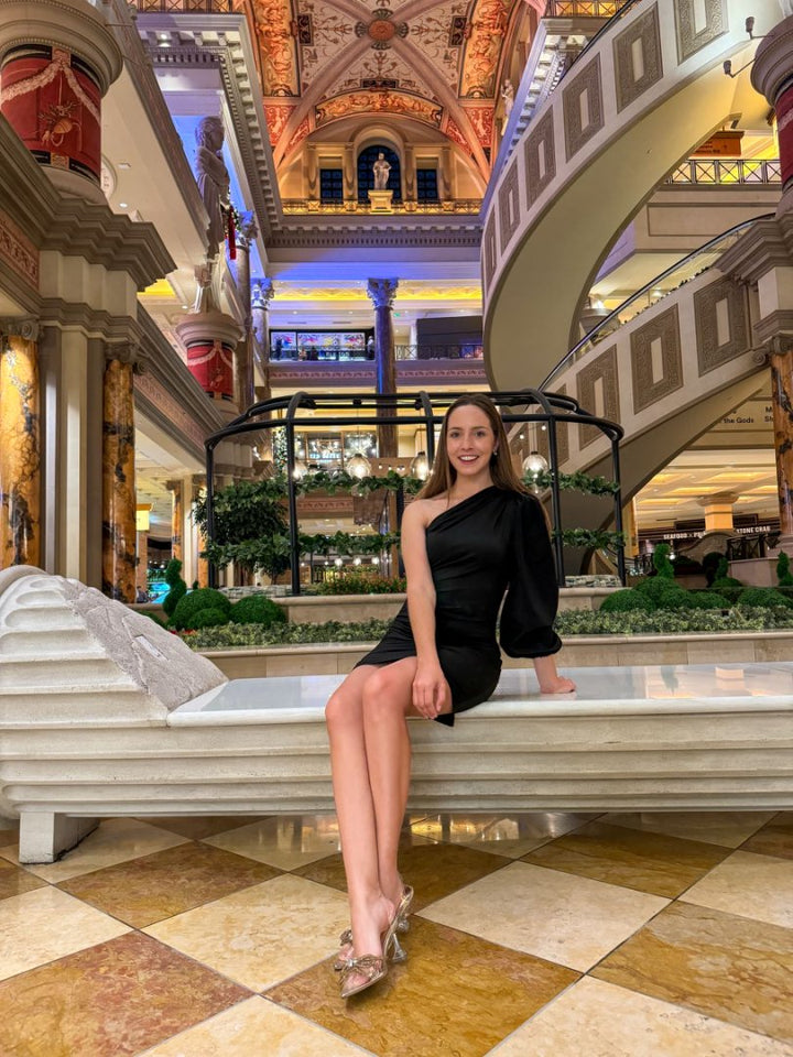 Woman in a black dress sitting on a bench in a luxurious mall interior.#color_gold