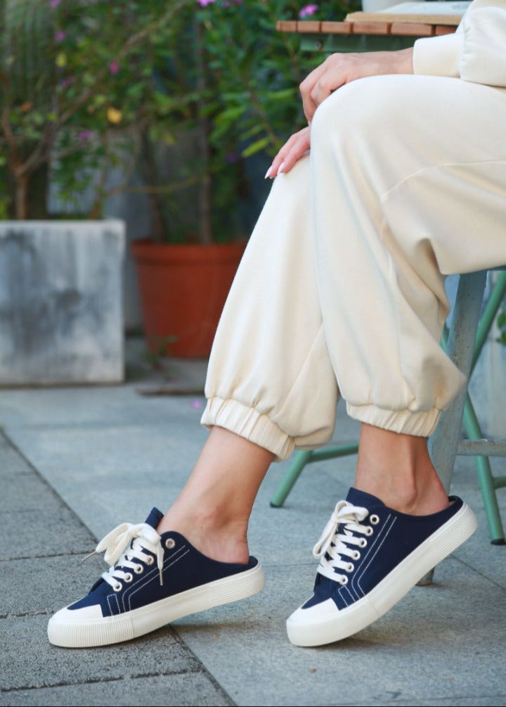 Person wearing navy blue sneakers with white laces on a patio with plants in the background#color_blue