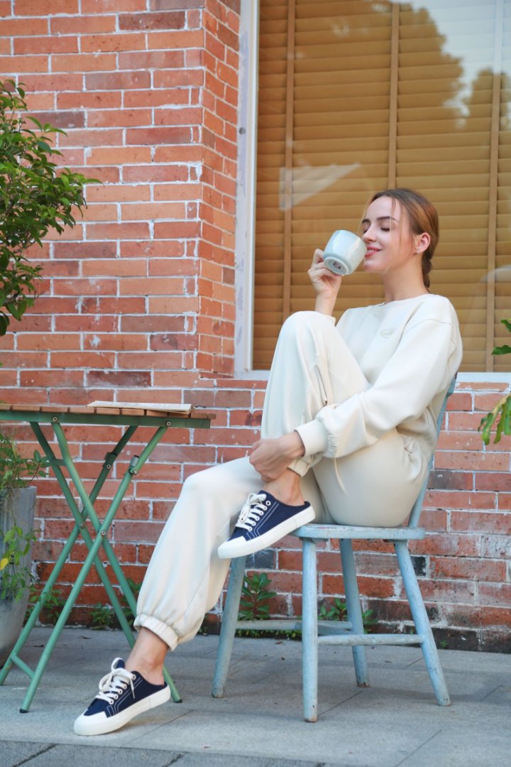 Woman sitting on a chair outdoors, drinking from a cup.#color_blue