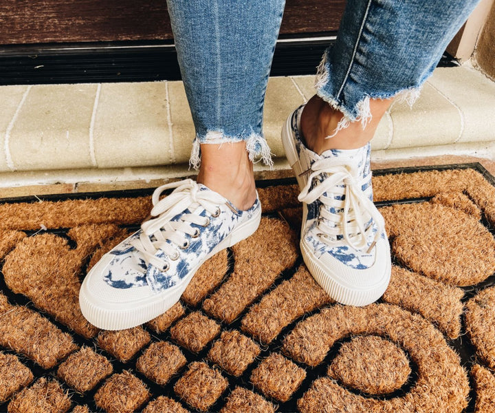 Person wearing floral sneakers on a doormat#color_dark-blue-tie-dye