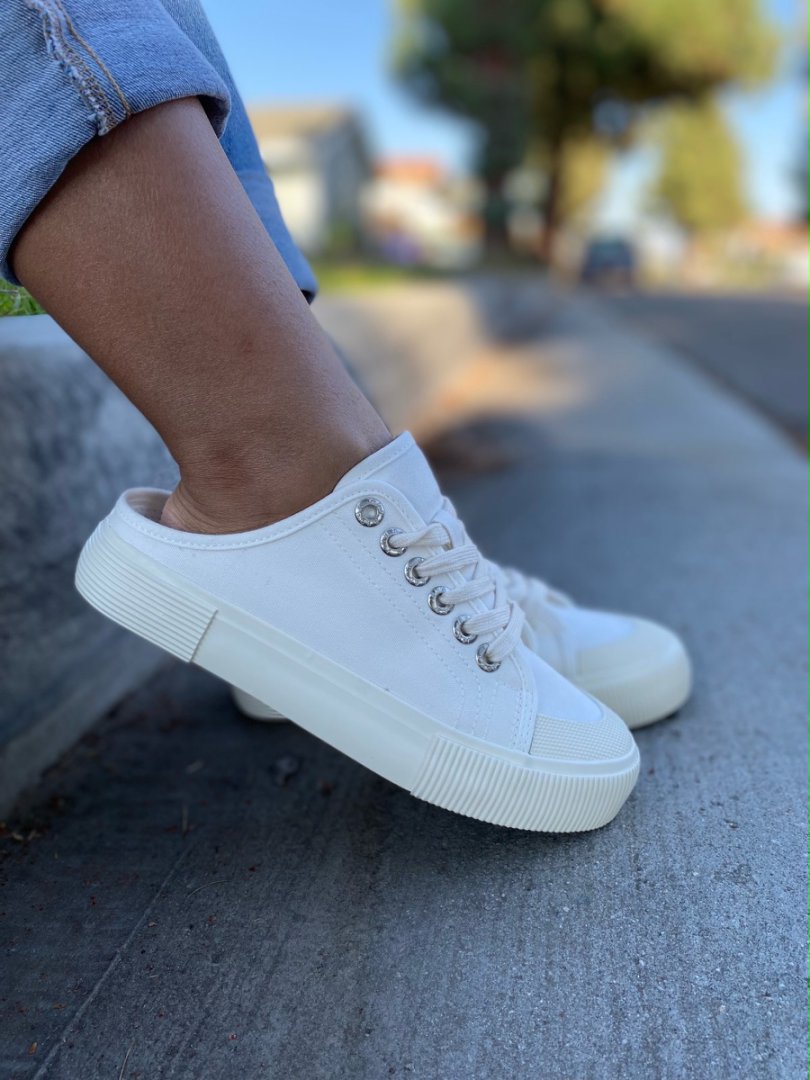 White sneakers worn on a concrete surface with a blurred background#color_white