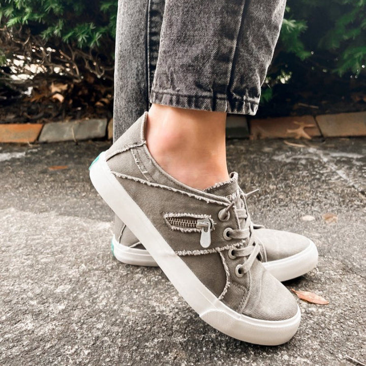 Person wearing gray high-top sneakers with white soles on a pavement background#color_grey