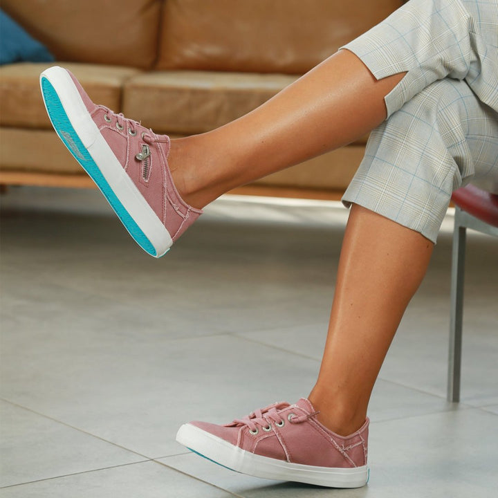 Person wearing pink sneakers with white soles and turquoise accents, sitting on a chair.#color_pink