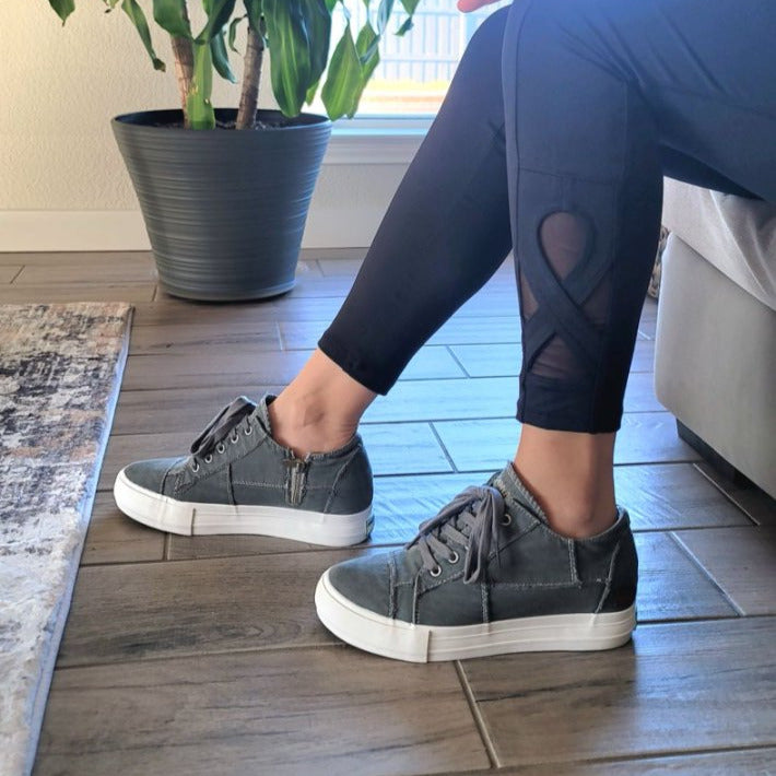 Person wearing dark blue leggings with a heart design and gray sneakers indoors.#color_grey