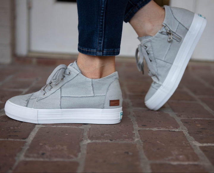 Gray sneakers worn on a brick floor#color_light-grey