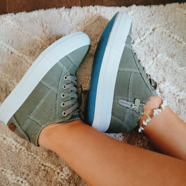 Green high-top sneakers with white soles on a carpeted floor#color_olive