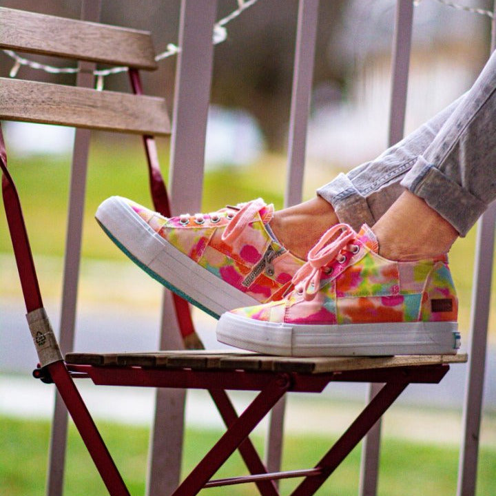 Colorful polka dot sneakers worn by a person sitting on a wooden chair outdoors.#color_orange