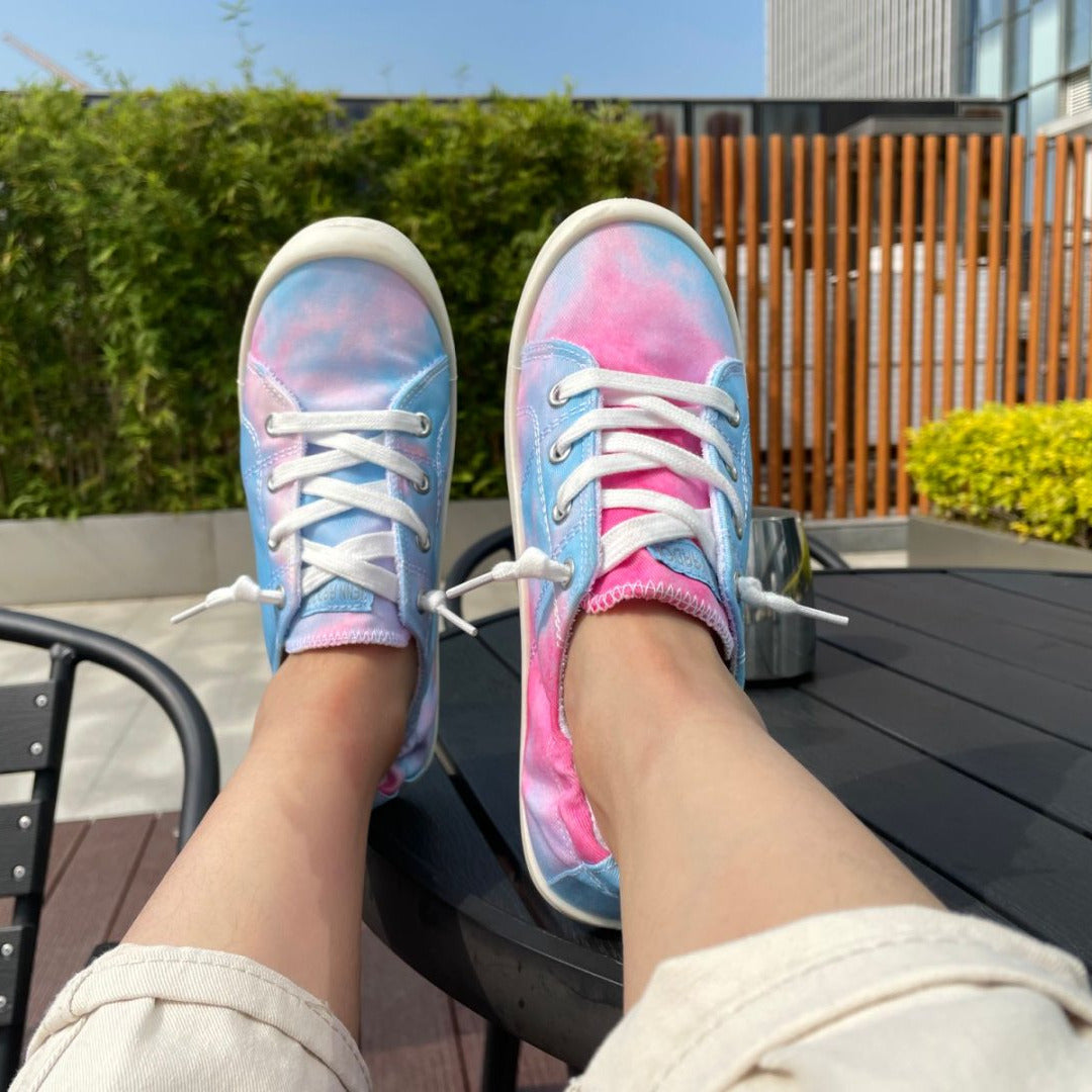 Person wearing tie-dye sneakers with a garden and building in the background