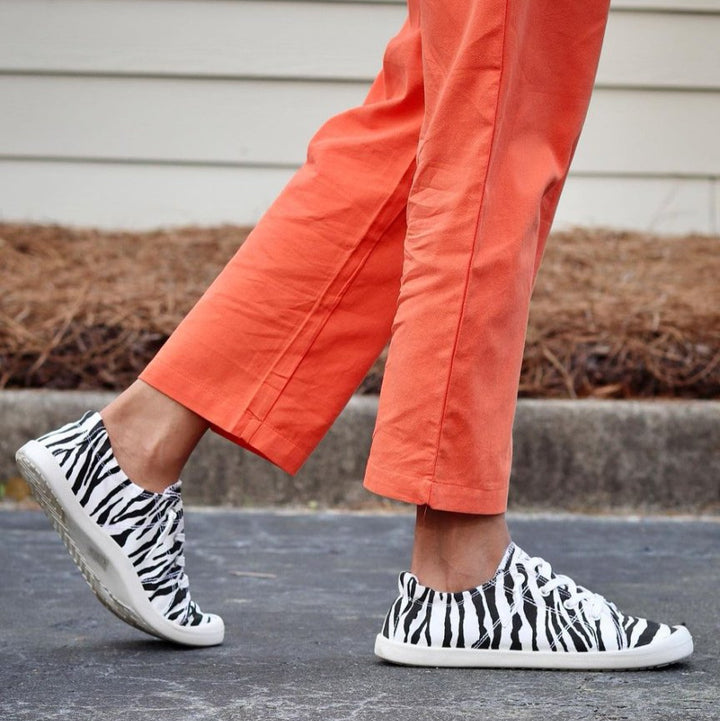 Person wearing zebra-striped shoes and orange pants on a concrete surface.#color_zebra