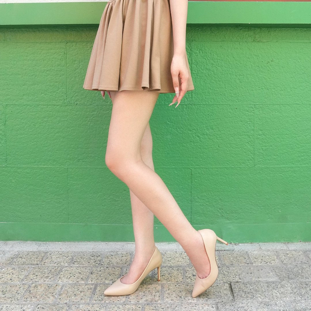 Person wearing a beige skirt and high heels against a green #color_natural