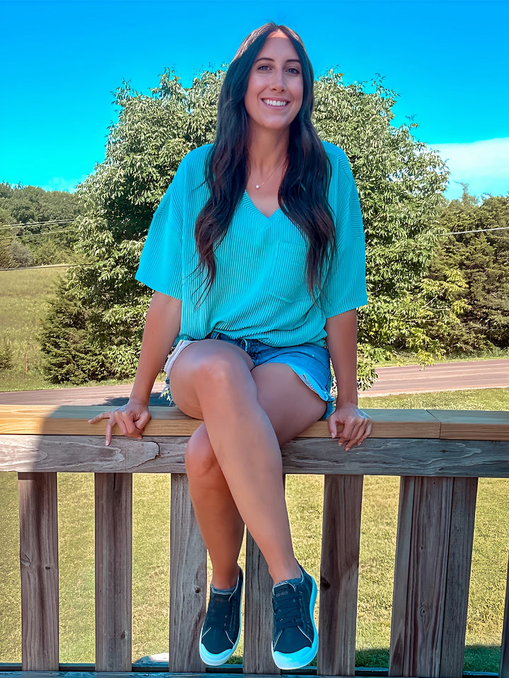Woman sitting on a wooden railing with a scenic background of trees and open space.#color_dark-grey