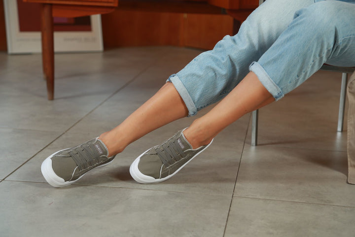 Person wearing gray sneakers with white soles on a tiled floor.#color_grey